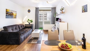 A modern living room with a sofa, coffee table, and dining area with a bowl of fruit and wine.