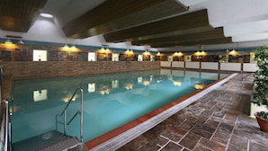 An indoor swimming pool with a stone wall, wooden ceiling beams, and a tiled floor.