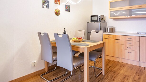 Cocina compacta con mesa de comedor, sillas, microondas y refrigerador pequeño.