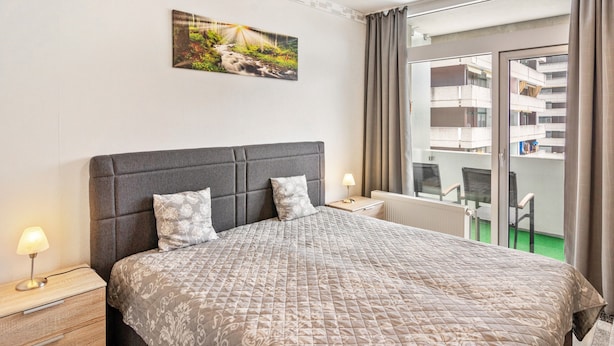 A hotel room with a large bed, a nightstand, a lamp, a painting on the wall, and a view of the outside balcony.