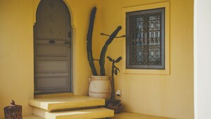 A yellow door with a metal gate, a potted plant, and a window with decorative bars. - Riad Lamp (Nanjo)