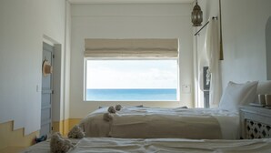 A bedroom with a large window overlooking the sea, a bed, a bedside table, and a lamp. - Riad Lamp (Nanjo)
