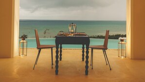 A dining table with chairs set up in a room with an arched doorway leading to a view of the ocean. - Riad Lamp (Nanjo)
