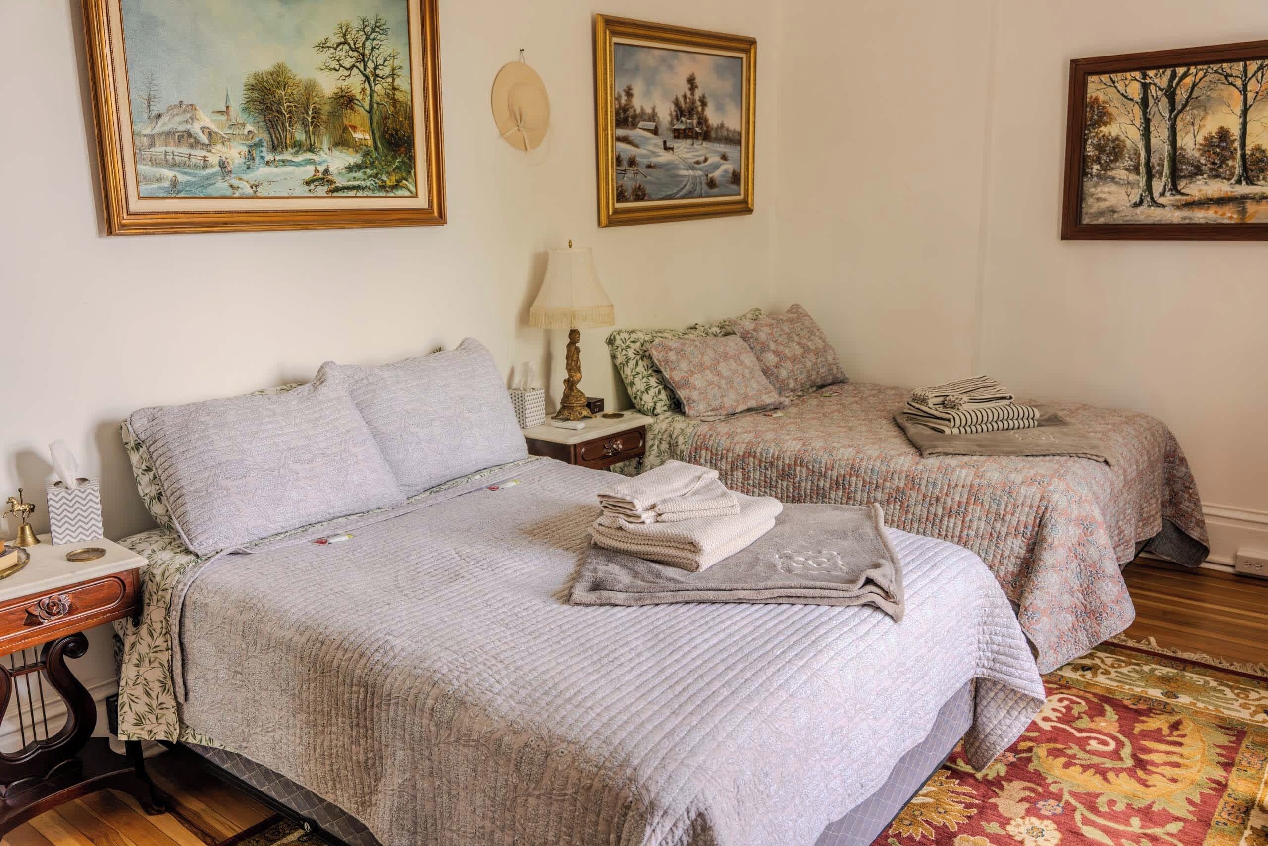 Quarto de hotel com duas camas, uma mesa de cabeceira, uma luminária e um tapete.