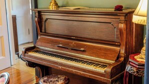 A grand piano in a room with a mirror, a lamp, and a decorative item on the piano. - The Gould Residence (Seneca Falls)