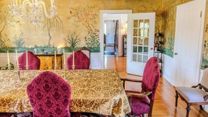 A dining room with a chandelier, floral wallpaper, and a view into another room. - The Gould Residence (Seneca Falls)