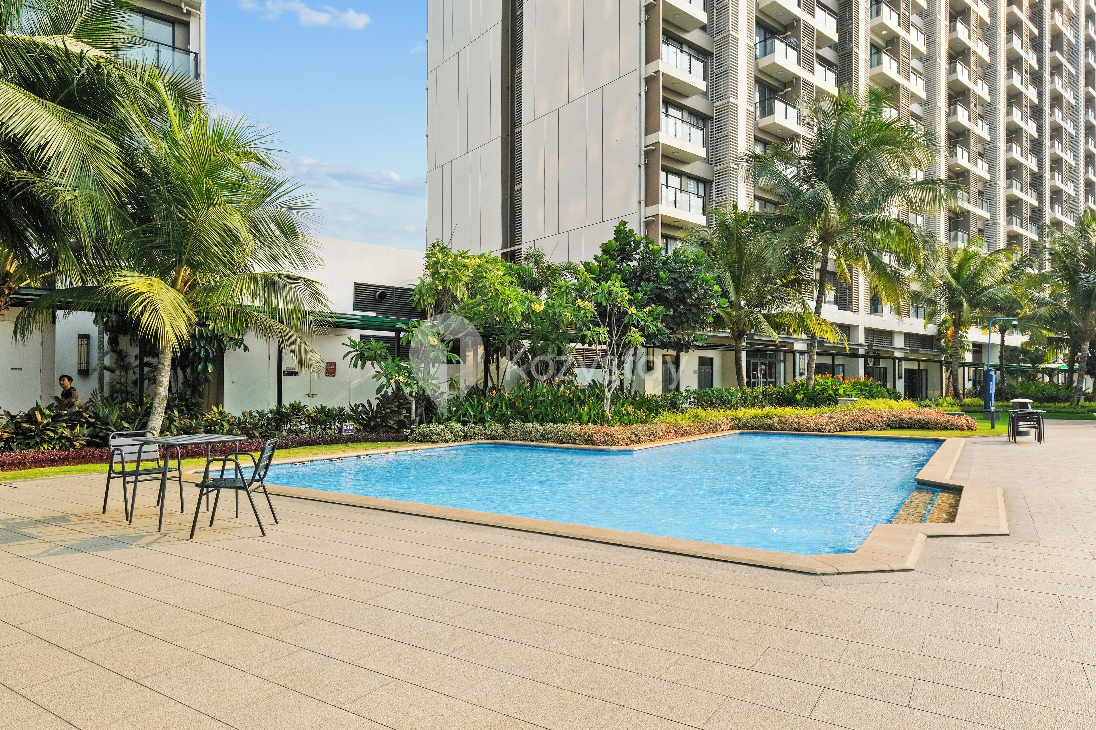 A swimming pool surrounded by palm trees and greenery, with a modern building in the background.