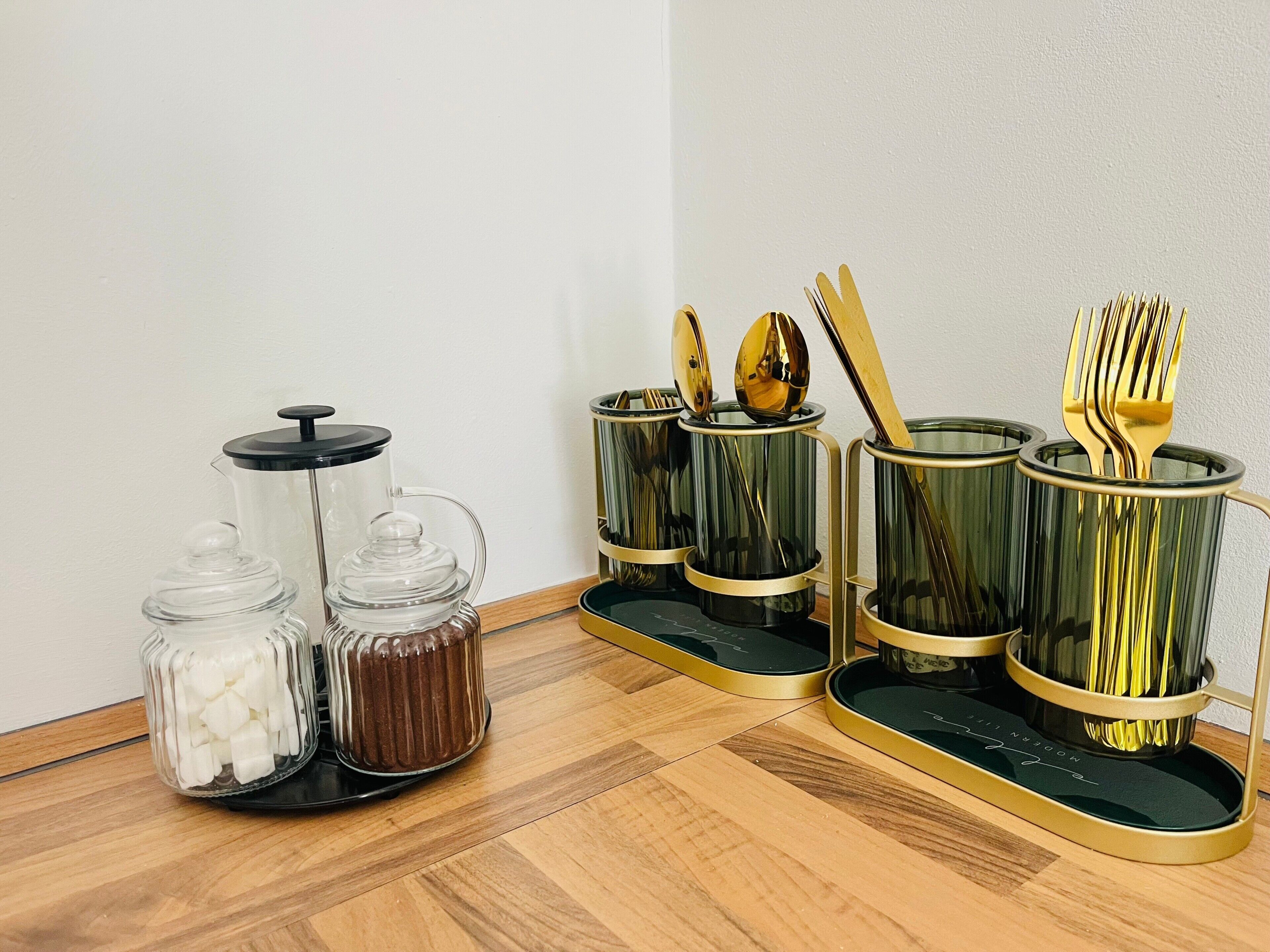 Un angolo cottura con una macchina da caffè, due barattoli di vetro e un portaposate con un cucchiaio e una forchetta.