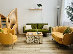 A living room with a green sofa, two yellow armchairs, a wooden coffee table, and a staircase.