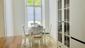 Een keuken met een eettafel, stoelen, een kast en een raam met jaloezieën.