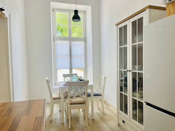 A kitchen with a dining table, chairs, a cabinet, and a window with blinds.