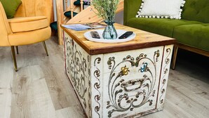 Een houten bijzettafeltje met een decoratief blad, een vaas met bloemen en een afstandsbediening erop.