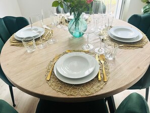 Une table de salle à manger ronde, avec de l’assiette blanche, des couverts dorés et des verres à vin transparents.