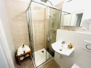 Une salle de bain moderne avec une douche à parois de verre, un lavabo blanc et une étagère en bois où sont posées des serviettes.
