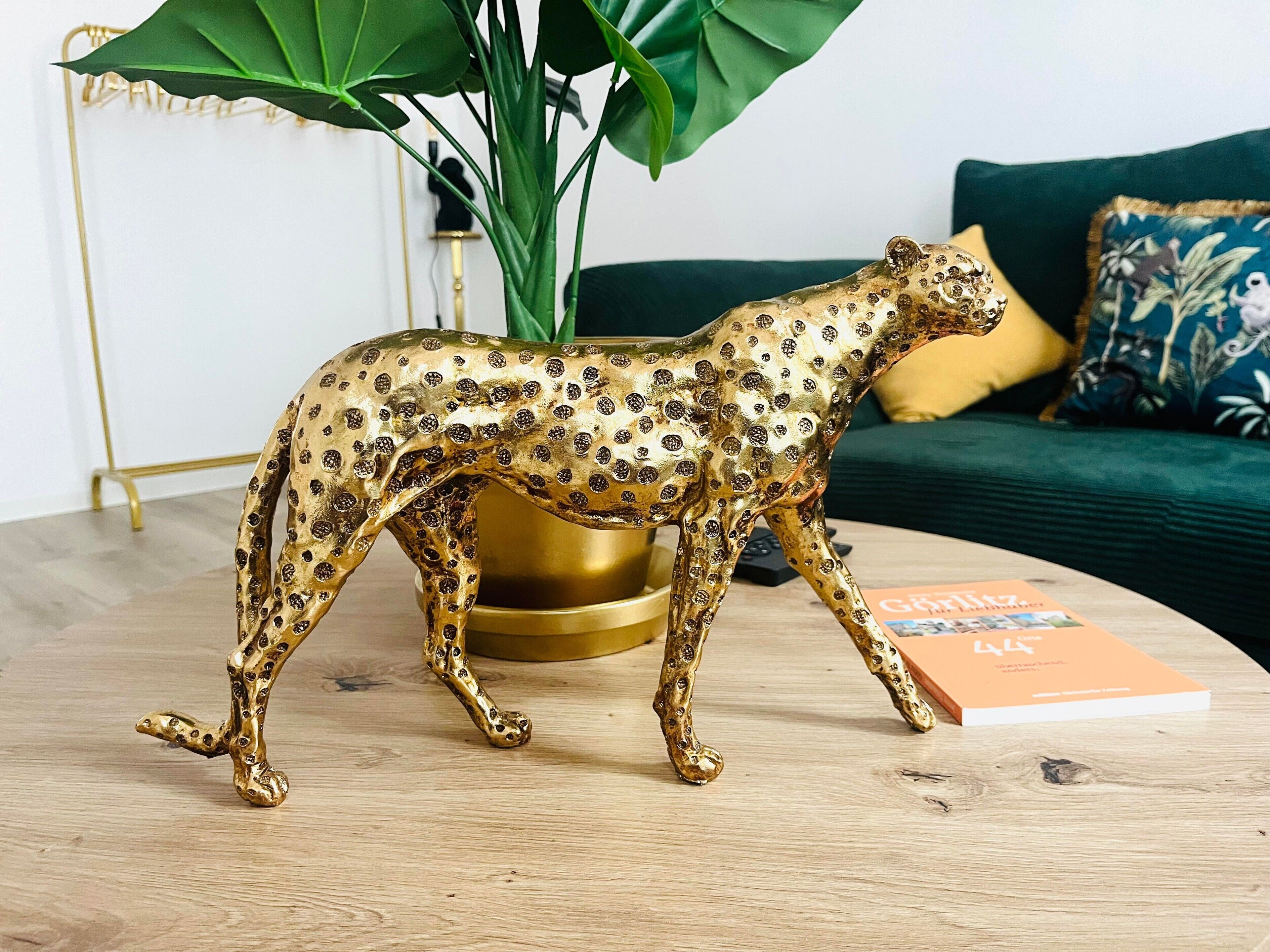 A leopard figurine on a wooden table with a book and a green plant in the background.