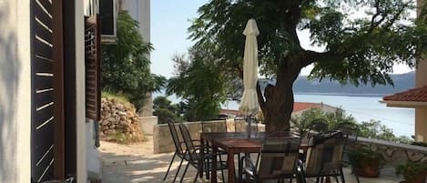 An outdoor patio with a table and chairs, a tree, and a view of a body of water and a building in the background.