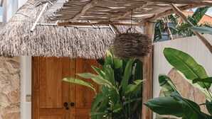 A thatched-roof entrance with a wooden door, a woven basket hanging above, and a bench with a cushion. - the macan Canggu (Canggu)