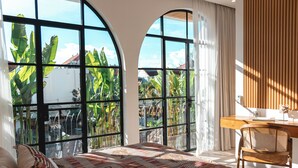 A bedroom with large arched windows, a bed with patterned bedding, a wooden desk, and a chair. - the macan Canggu (Canggu)