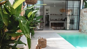 Un espace piscine extérieur moderne, agrémenté d’un mur en pierre, d’un panier en osier et d’un tabouret en bois.