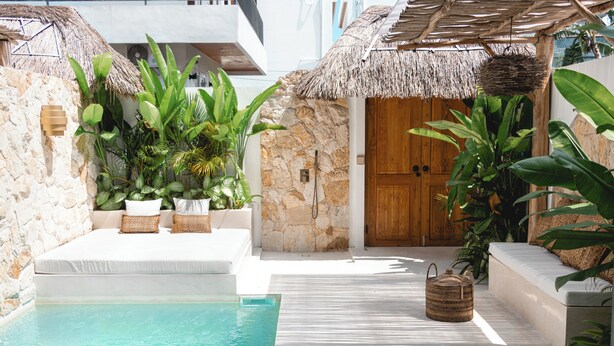 A pool area with a stone wall, a wooden door, and a thatched roof structure. - the macan Canggu (Canggu)