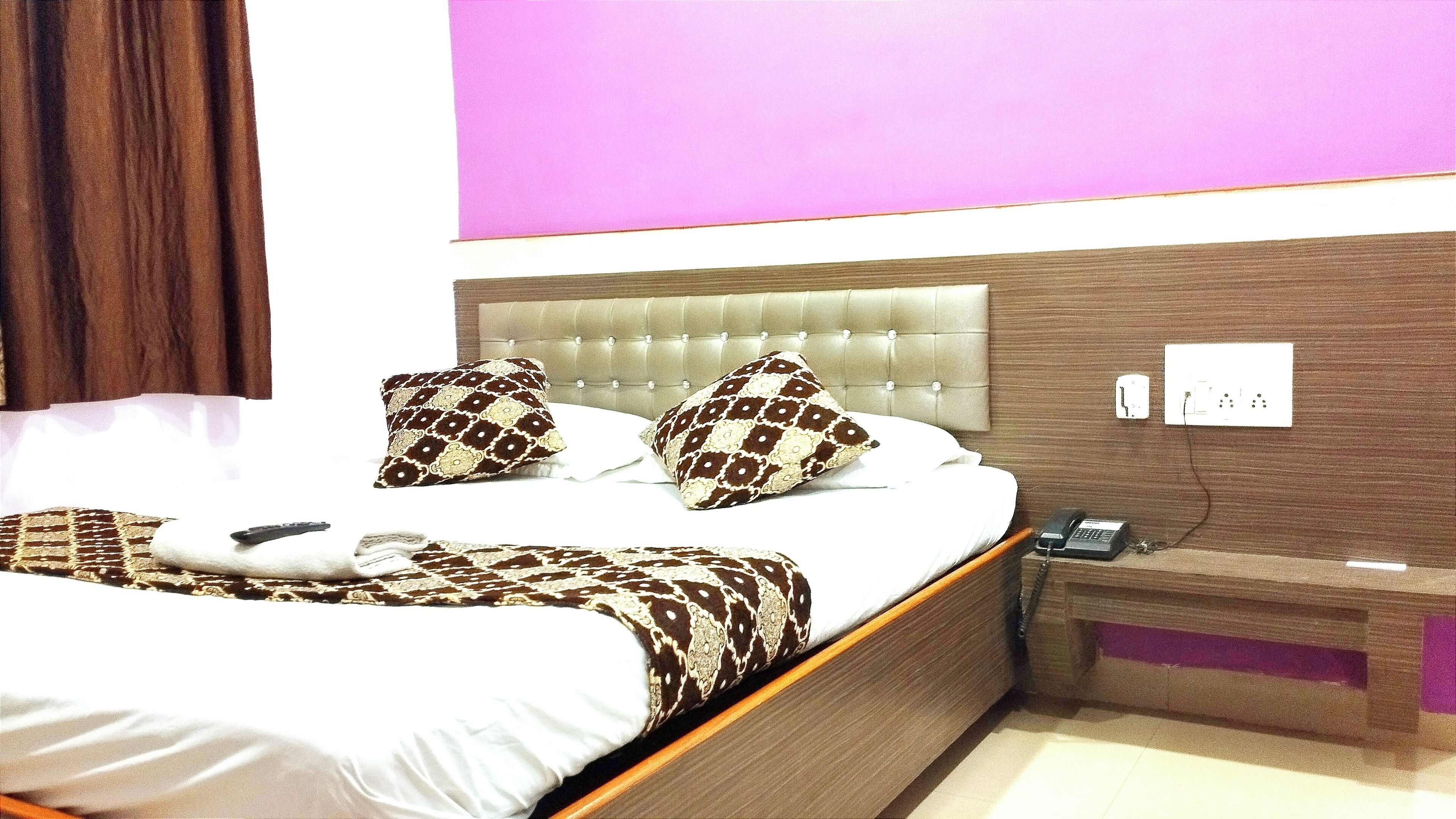 A hotel room with a bed, two patterned pillows, a bedside table with a phone, and a wall socket.