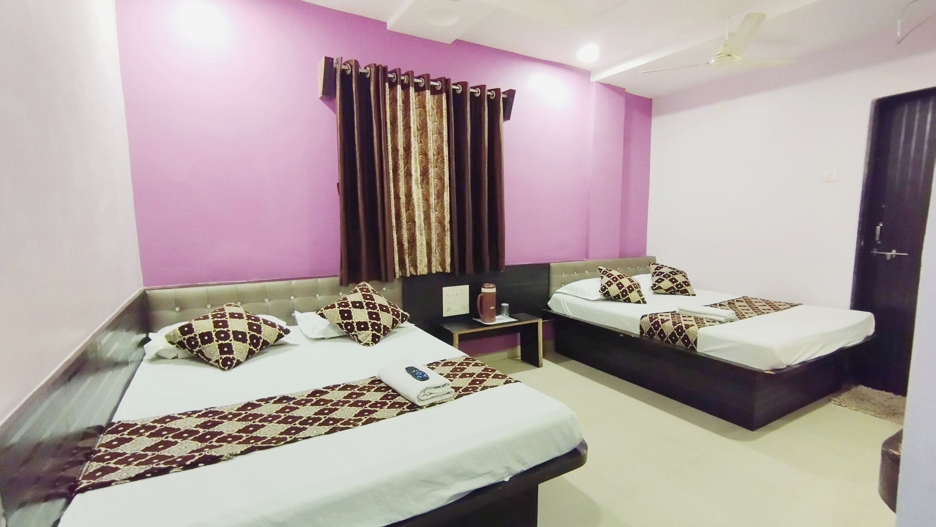 A hotel room with two beds, a nightstand, a coffee maker, and a window with curtains.