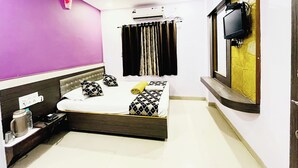 A hotel room with a bed, a ceiling fan, an air conditioner, a TV mounted on the wall, and a window with a view of the outside. - sai balaji residency (Rahata)