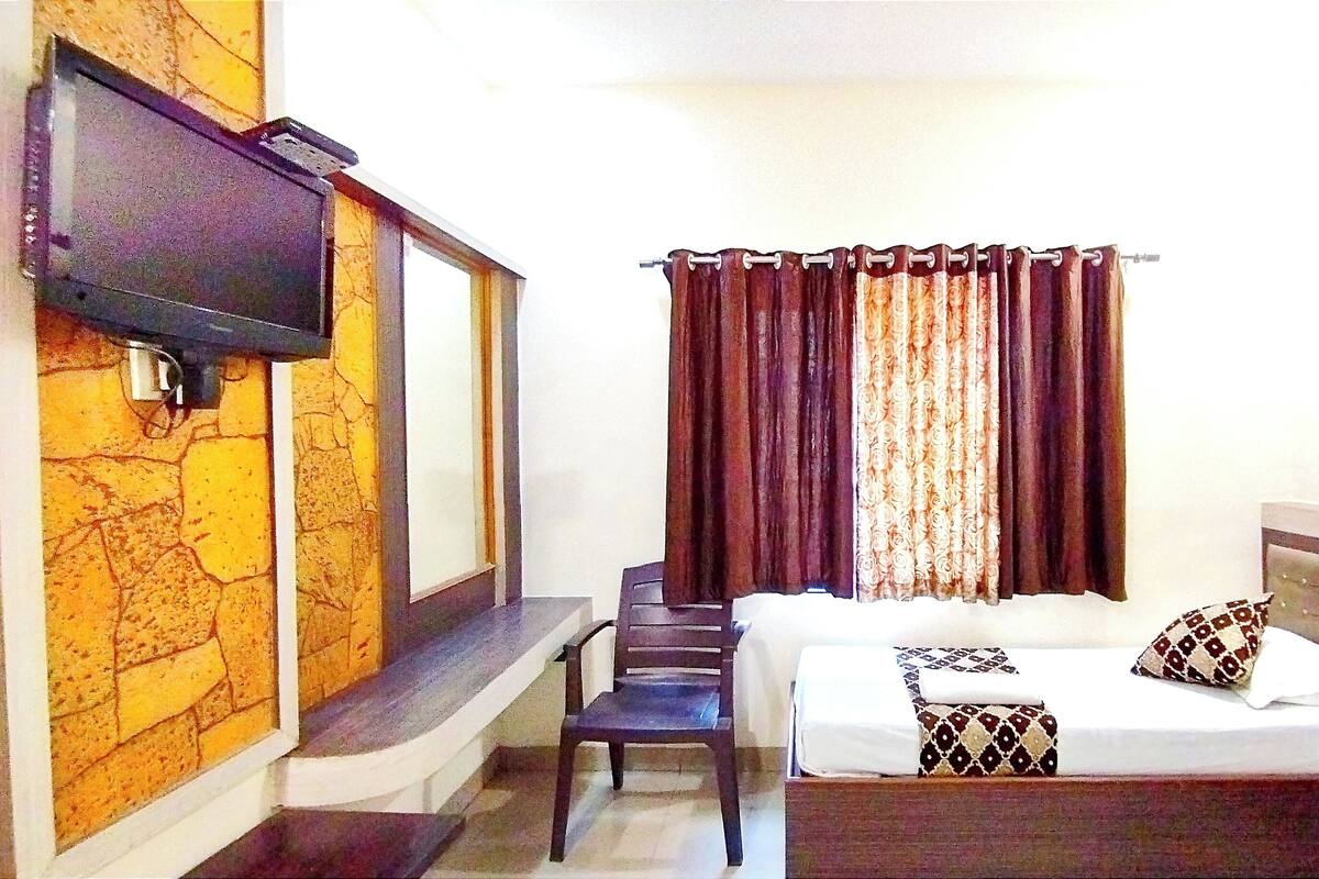 A hotel room with a bed, a TV mounted on the wall, a desk, and a chair.