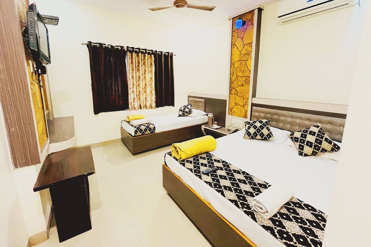 A hotel room with two beds, a ceiling fan, an air conditioner, a TV, and a window with curtains.