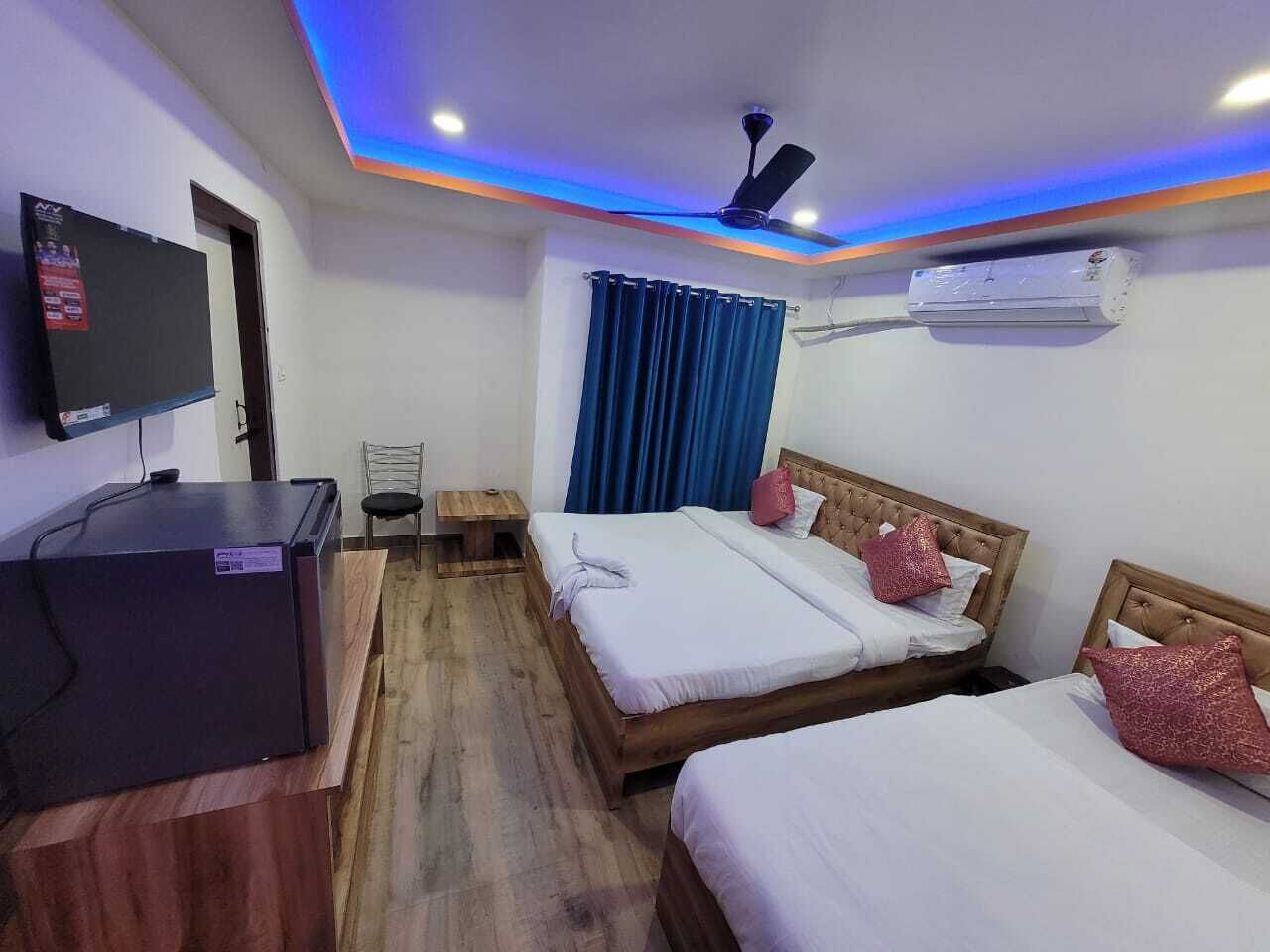 A hotel room with two beds, a desk with a computer, a ceiling fan, and an air conditioning unit.