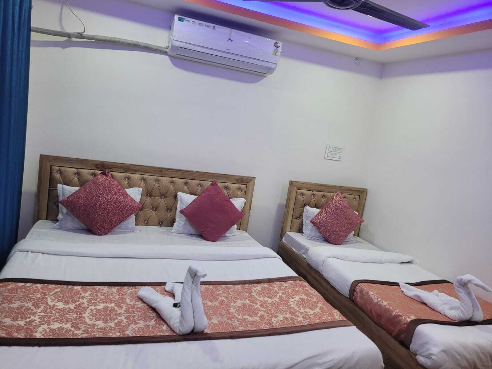 A hotel room with two beds, each with a wooden headboard, white bedding, and red decorative pillows. There is an air conditioning unit on the wall above the beds.