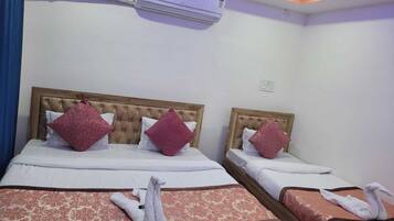 A hotel room with two beds, each with a wooden headboard, white bedding, and red decorative pillows. There is an air conditioning unit on the wall above the beds.