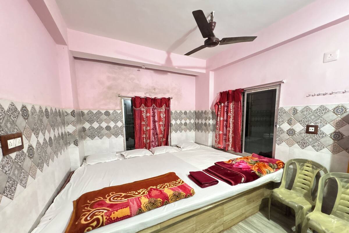 A bedroom with a bed, two chairs, a ceiling fan, and patterned walls.