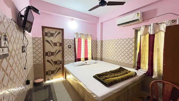 Un dormitorio con cama, ventilador de techo, aire acondicionado, televisor montado en la pared y mesita de noche.