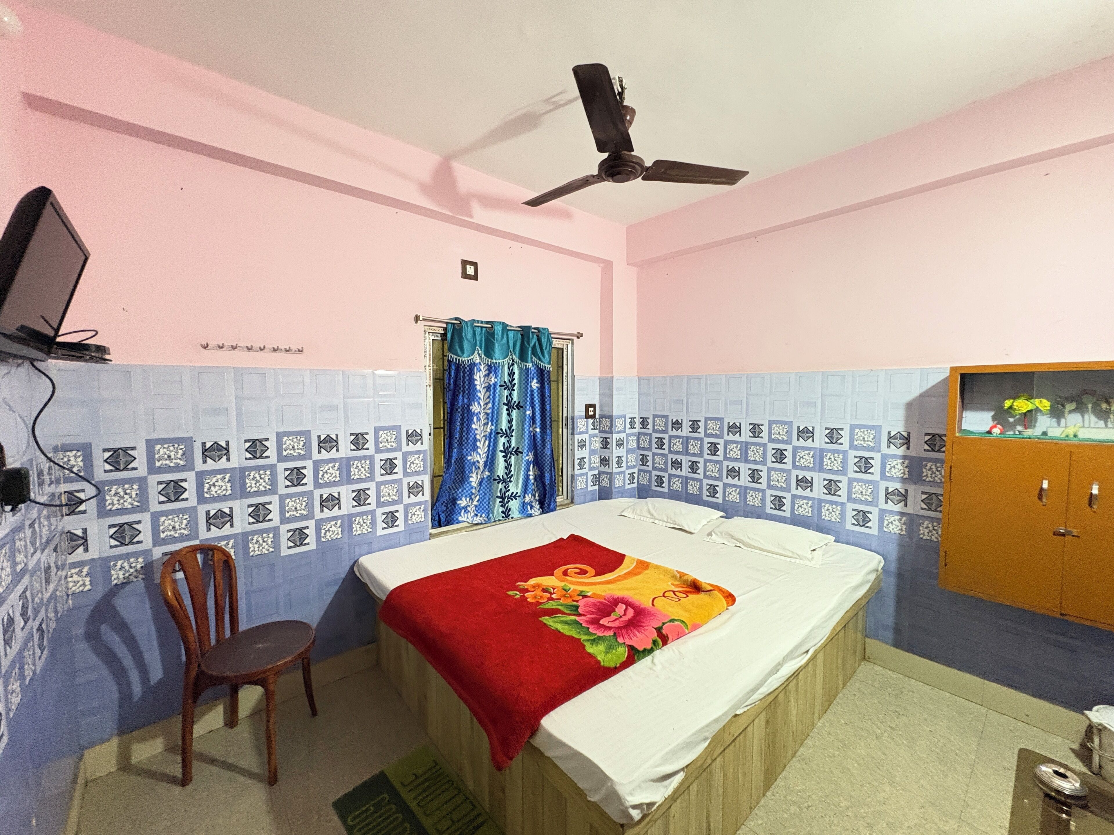 A bedroom with a bed, a chair, a ceiling fan, a wardrobe, and a window with curtains.