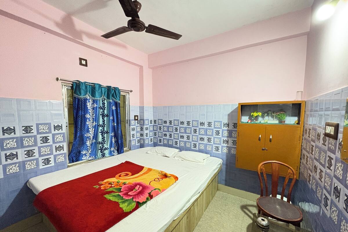 A room with a bed, a ceiling fan, a wooden cabinet, and a chair.
