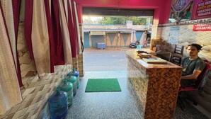Zona de recepción de hotel con mostrador de mármol, dispensadores de agua y un felpudo verde.