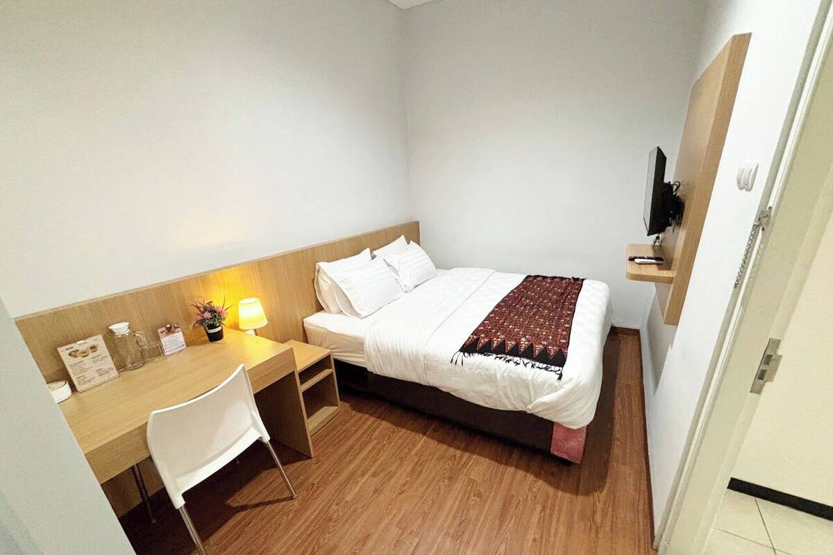 A small, neatly arranged bedroom with a bed, a desk, and a chair.