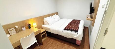 A small, neatly arranged bedroom with a bed, a desk, and a chair.