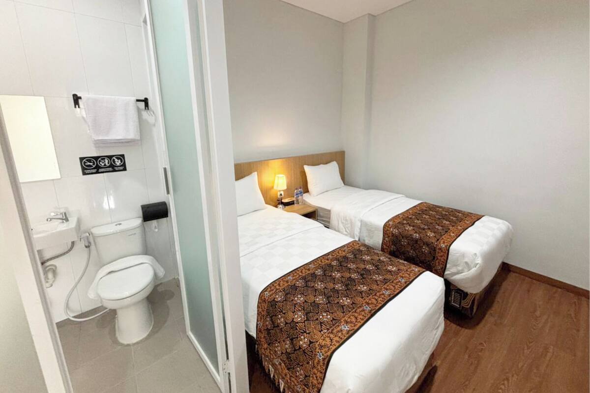 A hotel room with two beds, a bathroom with a toilet and sink, and a nightstand with a lamp.