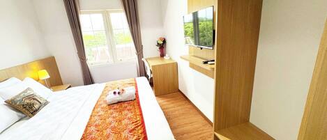 A hotel room with a bed, a TV mounted on the wall, a small desk, and a window with curtains.