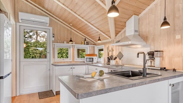 A modern kitchen with wooden ceiling beams, white cabinetry, a granite countertop, and a large island with a sink.