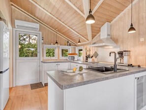Cocina moderna con vigas de madera en el techo, armarios blancos, encimera de granito y una isla grande con lavamanos.