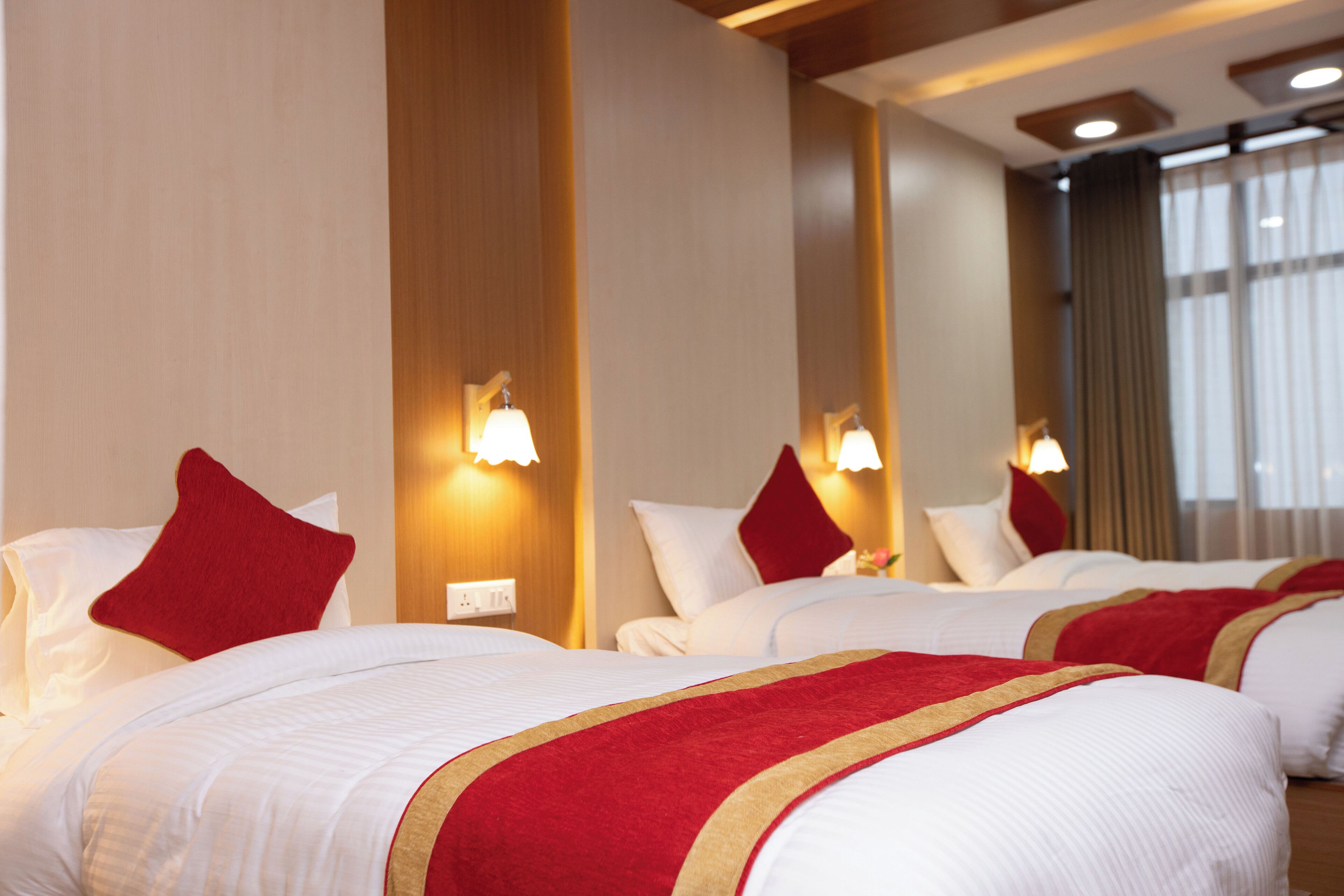 A hotel room with two beds, each with white bedding and red pillows, and wall-mounted lamps.