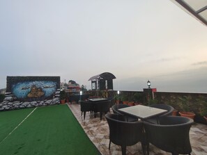 An outdoor patio area with a mural, outdoor seating, and a view of the cityscape. - Hotel Ambrosia (Bhimeshwar)
