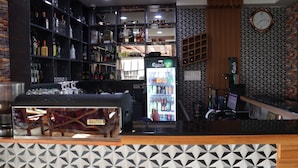 A bar area with shelves of liquor bottles, a minibar, and a minibar refrigerator stocked with beverages. - Hotel Ambrosia (Bhimeshwar)