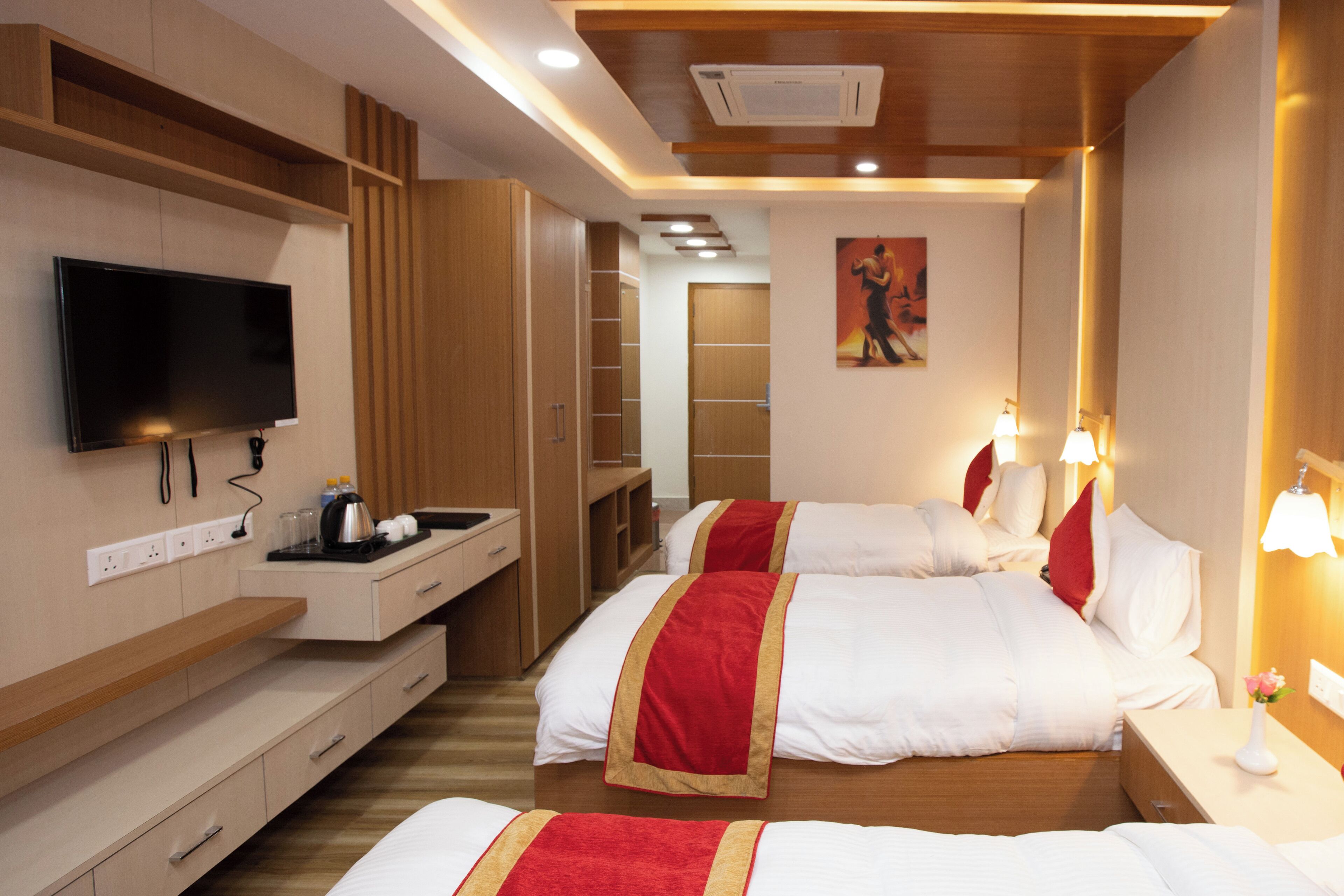 Habitación de hotel con dos camas, un televisor, un escritorio con tetera y un cuadro en la pared.