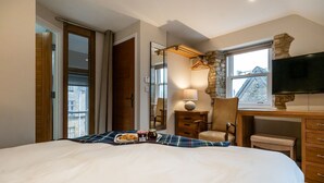 Une chambre à coucher comprenant un lit, une chaise, un bureau, un téléviseur et une fenêtre donnant sur des immeubles.