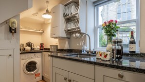 Une cuisine moderne équipée d’un lave-linge intégré, d’une machine à café et d’une fenêtre donnant sur un bâtiment historique.