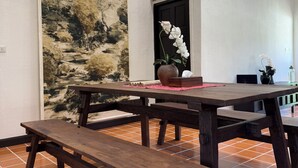 Un comedor con una mesa de madera y bancos, un tapiz grande en la pared y suelo de baldosas.